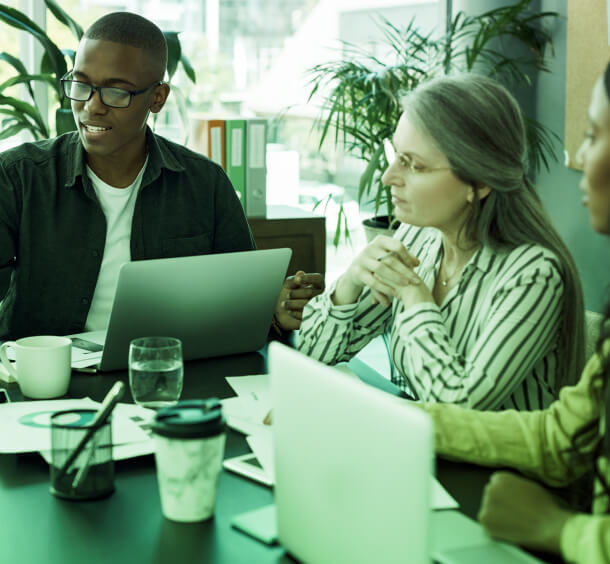 Three Public Relations consultants in Austin discuss strategy with laptops and papers, emphasizing Social Media and Crisis Management expertise.