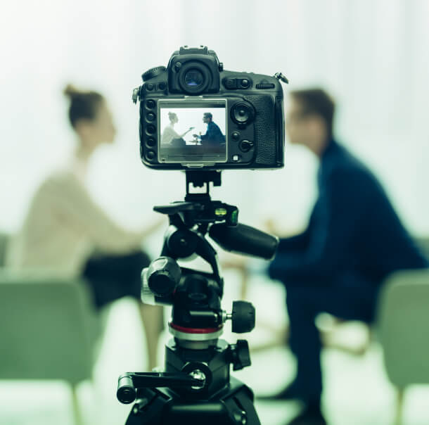 A DSLR camera on a tripod symbolizes Austin PR strategies as two people discuss Public Relations and Crisis Management consulting.