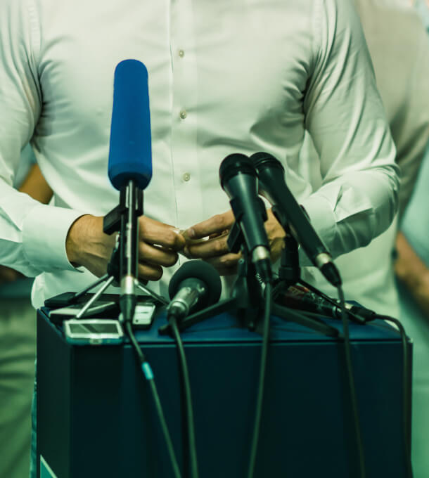A professional in a white shirt at a podium with microphones, exemplifying Austin Public Relations, Management, and Crisis Consulting expertise.