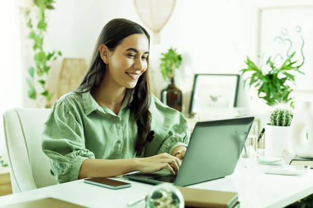 A person in a green shirt types on a laptop, embodying Austin PR expertise amid plants, focusing on Public Relations and Crisis Management.