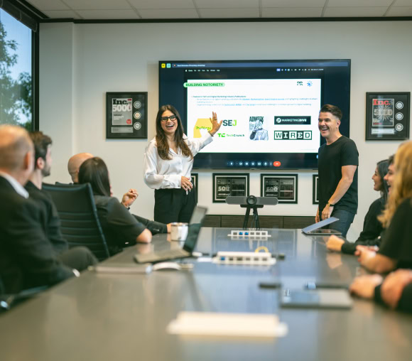A woman leads an Austin-based Public Relations meeting, showcasing crisis management on a screen to colleagues at a long table.