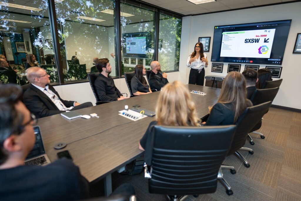 A woman leads a presentation on crisis management to a team in Austin at a conference table, with slides about PR and social media strategy.